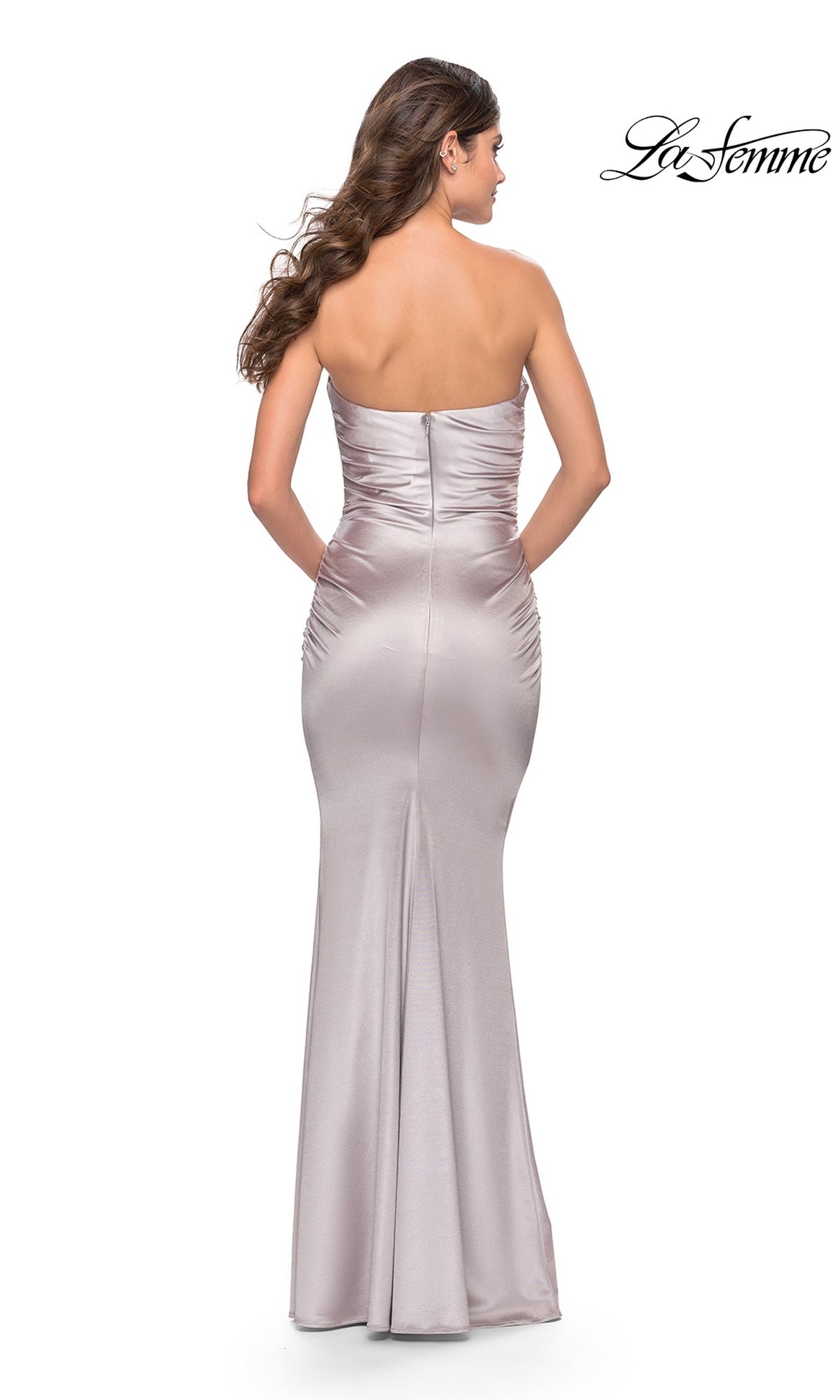 A woman in the Simple Strapless Long La Femme Prom Dress 31189, fitted and light lavender, stands facing away to highlight the elegant ruched detailing and floor-length evening gown design.